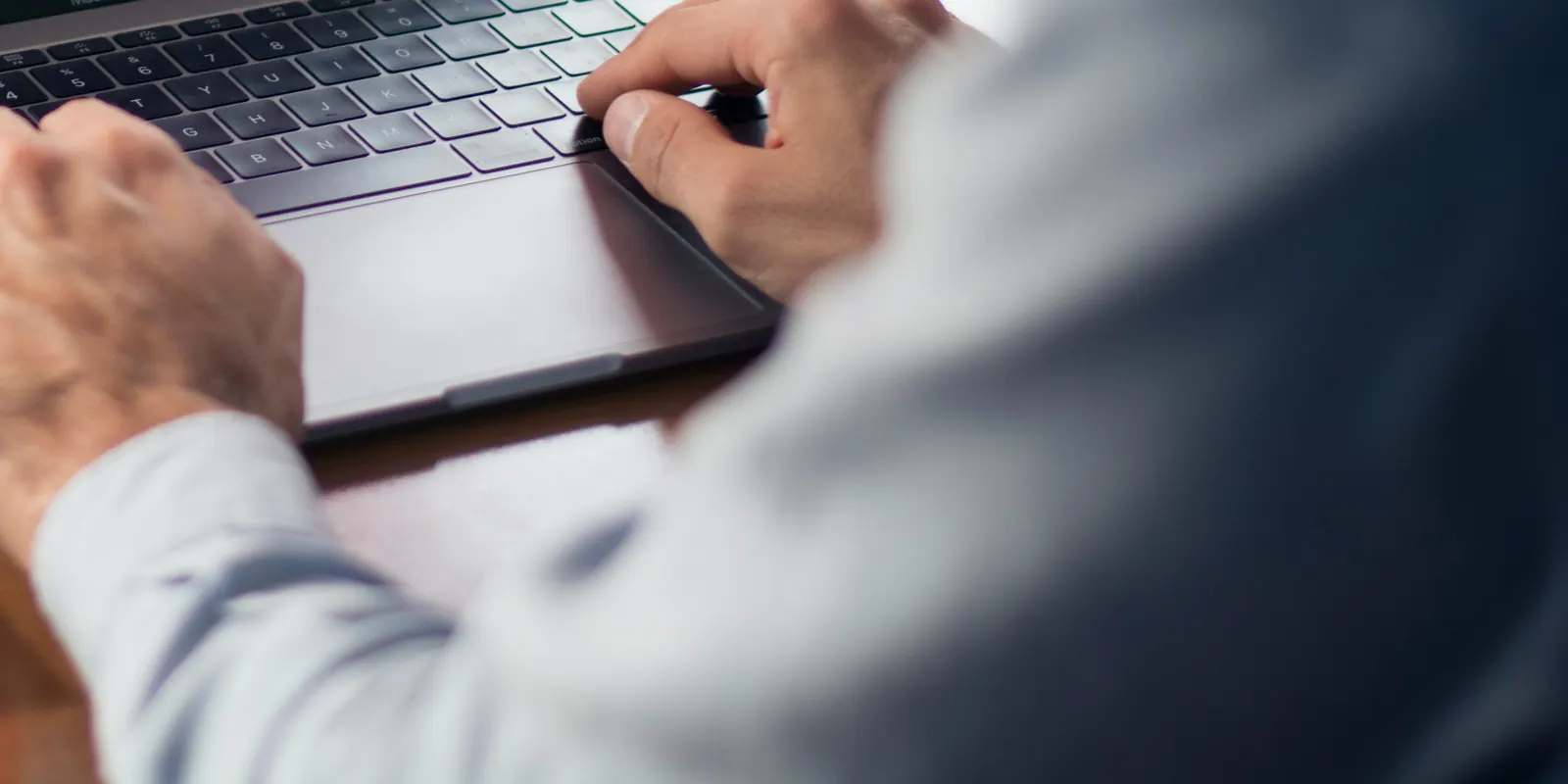 Hands on a laptop keyboard, seen over the shoulder of the person typing