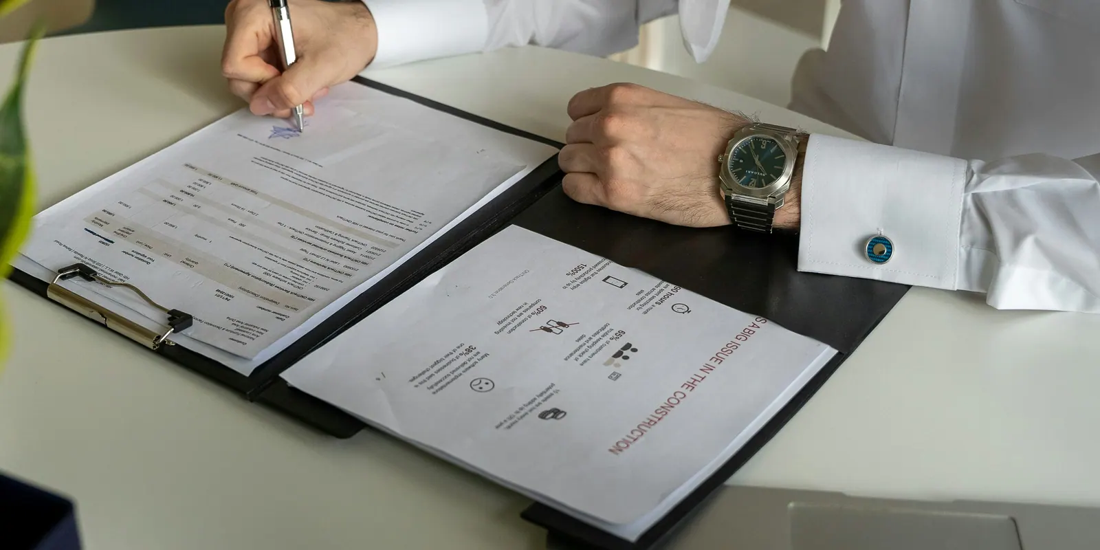A person in a white shirt signing a document on a clipboard at a white desk